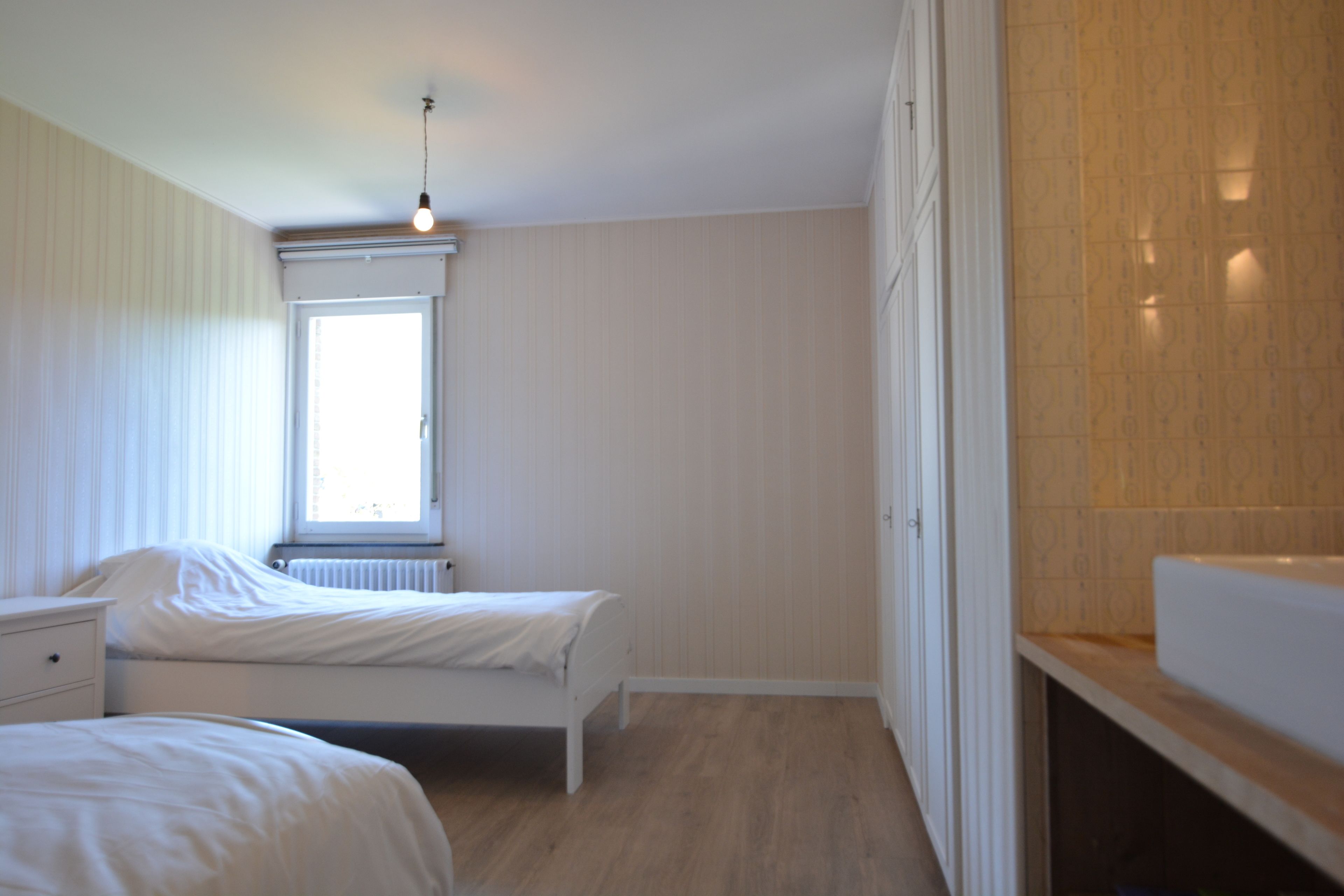 A bedroom with two beds, a window, and a radiator.