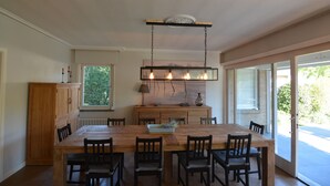 Un coin repas avec une table et des chaises en bois, un luminaire suspendu et une vue à travers une porte vitrée.