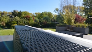 Une terrasse sur le toit, dotée d’un toit en métal à motifs, entourée d’une végétation luxuriante et d’arbres.