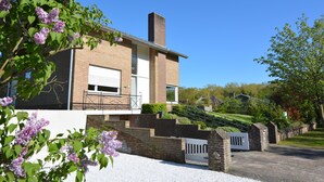 Une maison moderne à deux étages, avec une façade en briques, une cheminée et une porte de garage blanche.