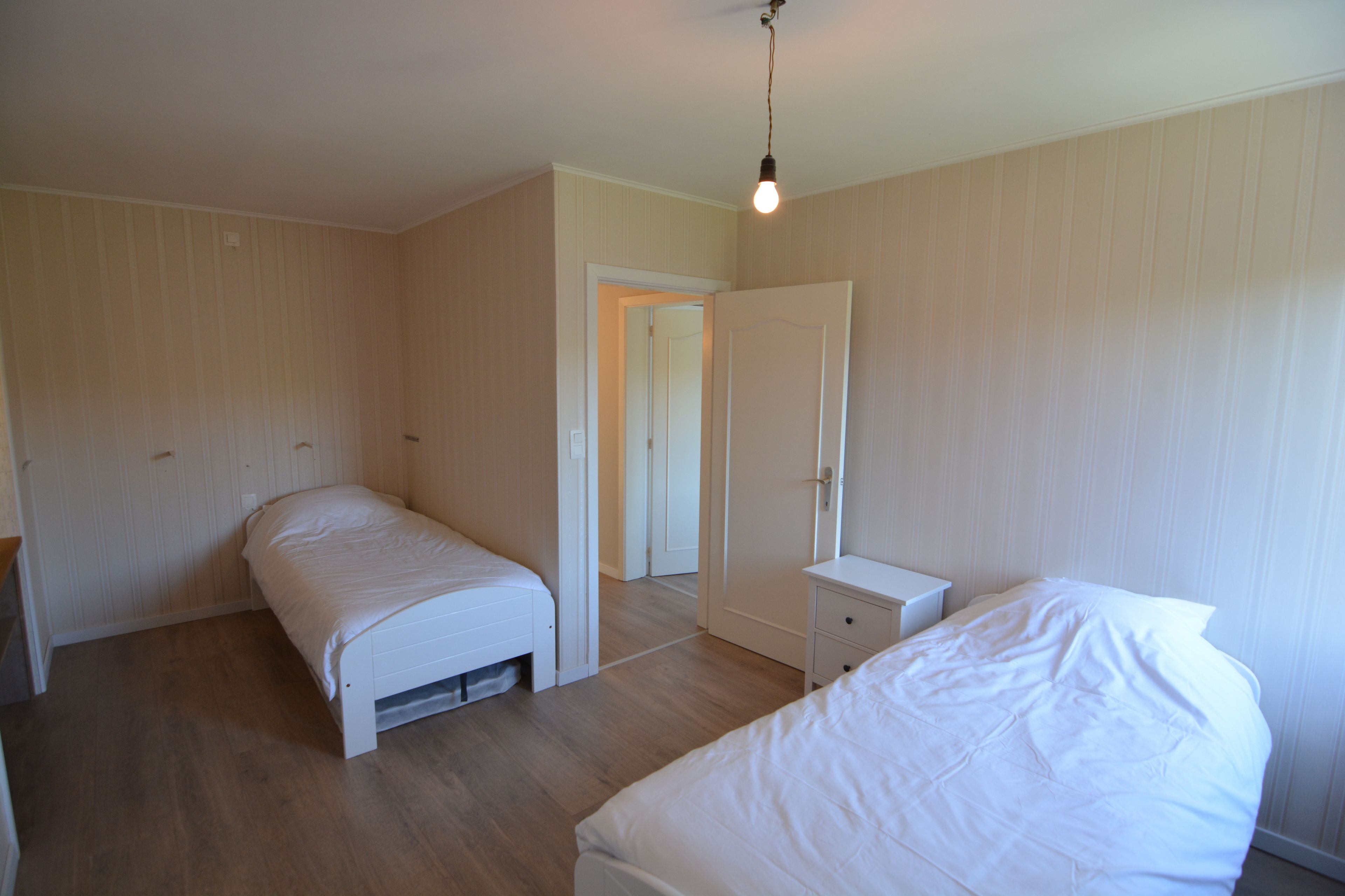 A bedroom with two beds, a nightstand, and a door leading to another room.