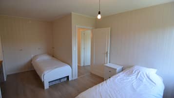 A bedroom with two beds, a nightstand, and a door leading to another room.