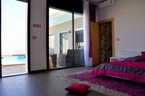 Un dormitorio moderno con una cama grande, vistas a una piscina y un ventanal corredero que da a un espacio exterior.