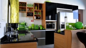 Una cocina moderna con electrodomésticos negros y verdes, repisas de madera con cristalería y un microondas integrado.