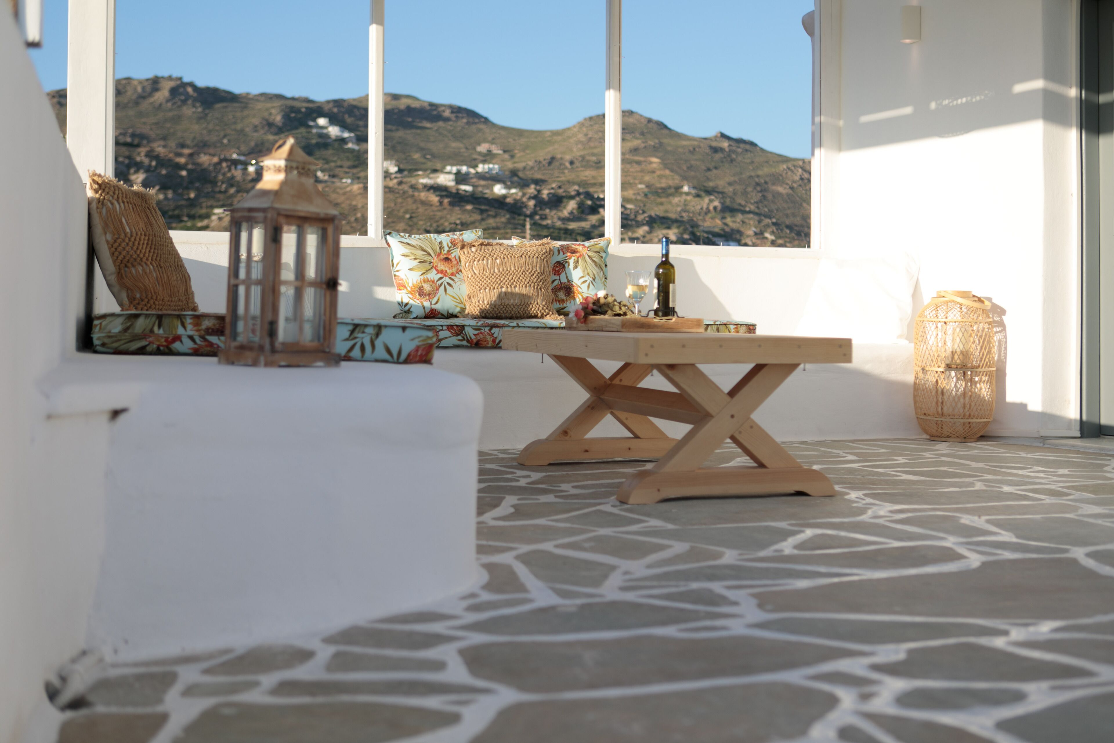 A terrace with a wooden table, wicker basket, and a view of mountains.