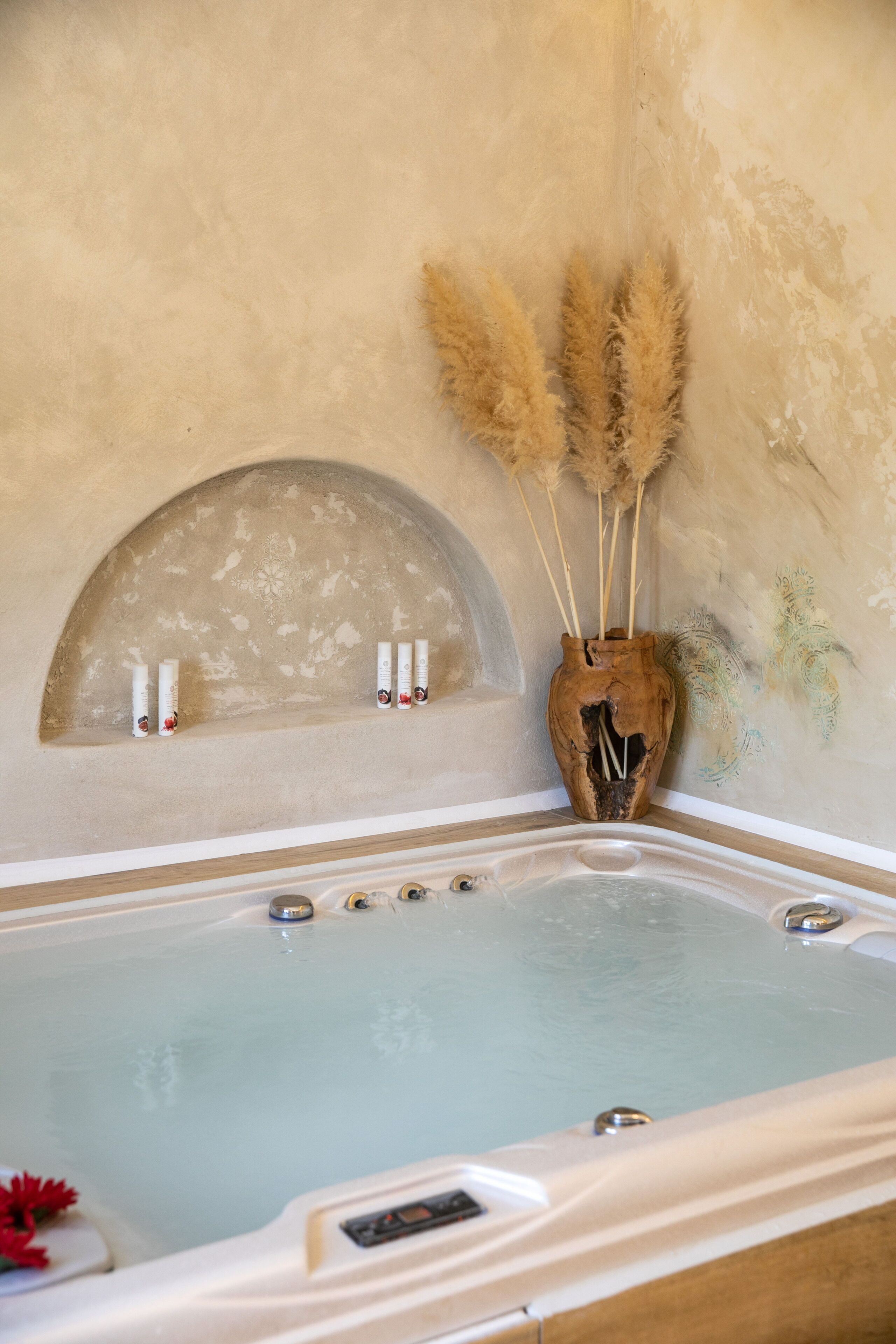 Un jacuzzi de diseño rústico, un jarrón decorativo con plumas de pampa y una pared con estampado floral.