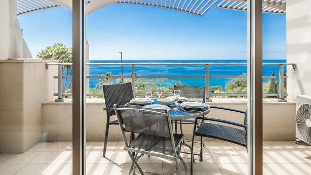 Un balcone con un tavolo e sedie in vetro, con vista sulla costa.