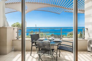 A balcony with a glass table and chairs, overlooking a coastal view. - Oceanside Terrace Apartment by Holiday Rental Management (Funchal)