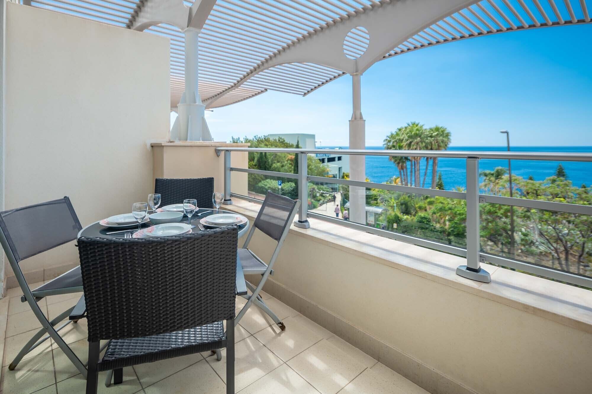 A balcony with a table set for two, overlooking a coastal view.