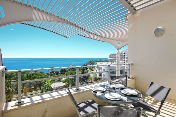 A balcony with a table set for dining, overlooking a coastal view. - Oceanside Terrace Apartment by Holiday Rental Management (Funchal)