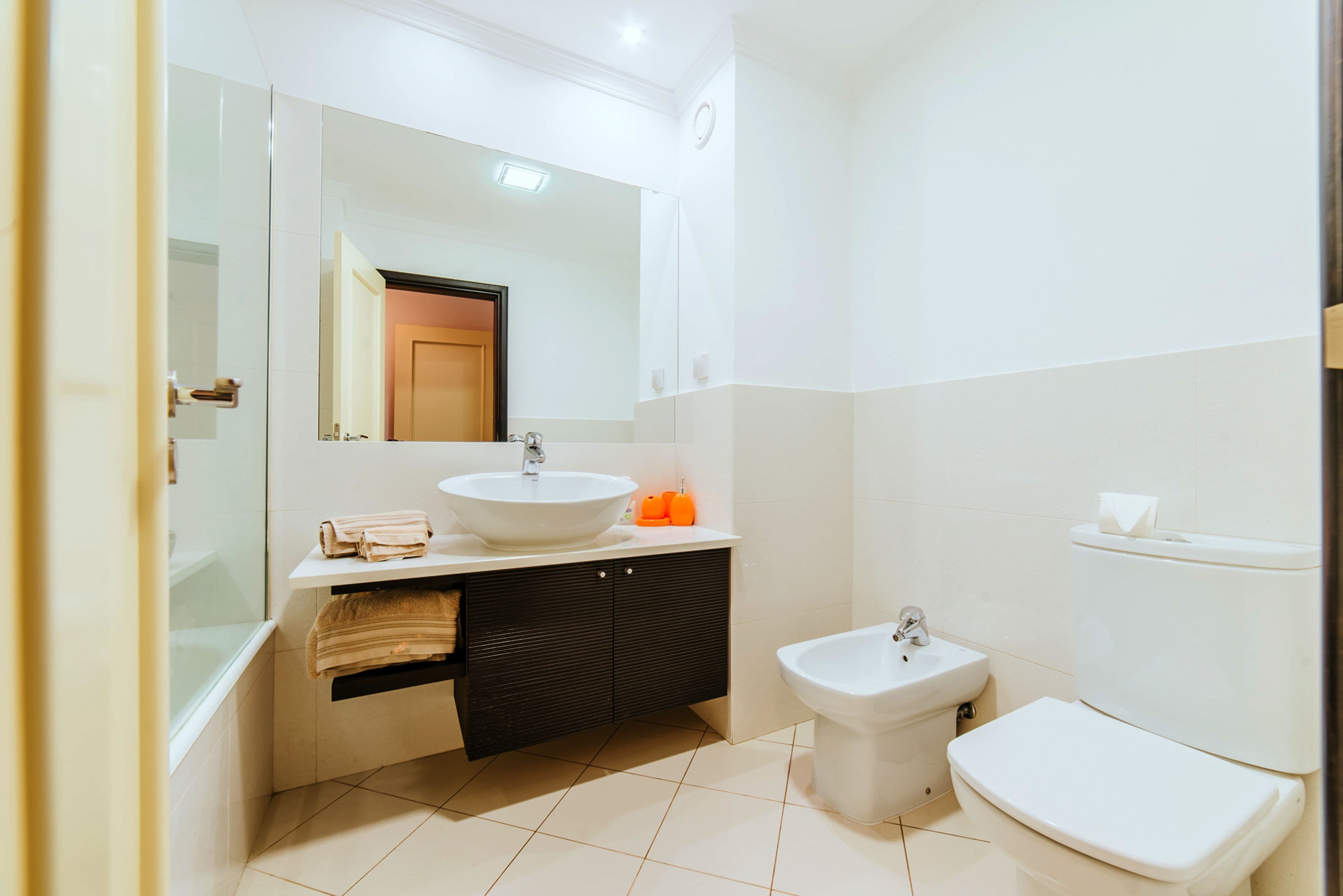 A modern bathroom with a large mirror, a sink, a bidet, and a toilet.
