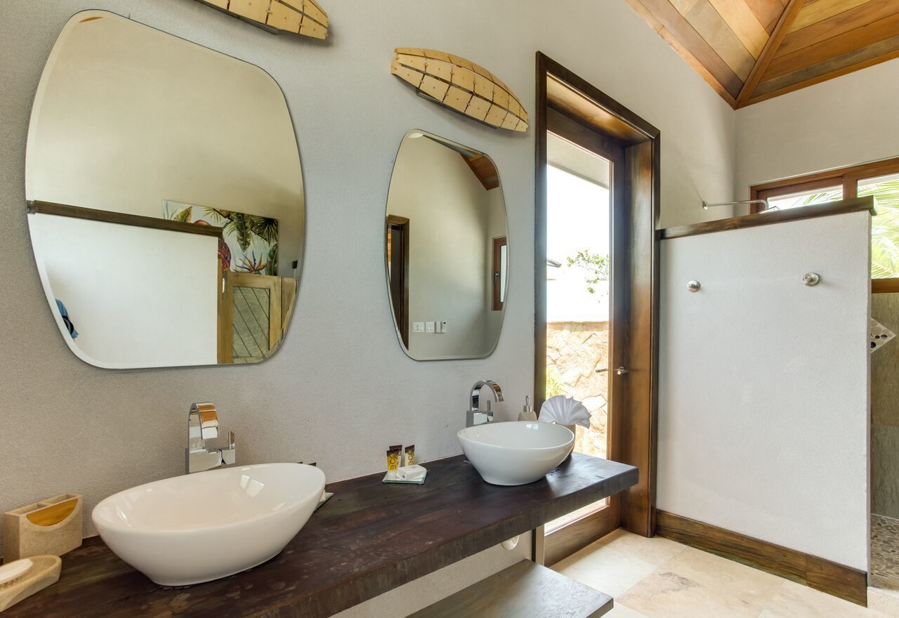 A bathroom with a large oval sink, two mirrors, a wooden countertop, and a shower area.