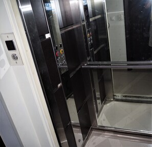 Interior de un ascensor con paredes metálicas, una barandilla y botones de control.