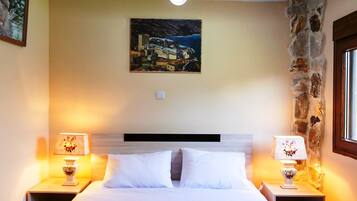 A hotel room with a bed, two bedside lamps, a painting on the wall, and a stone wall.