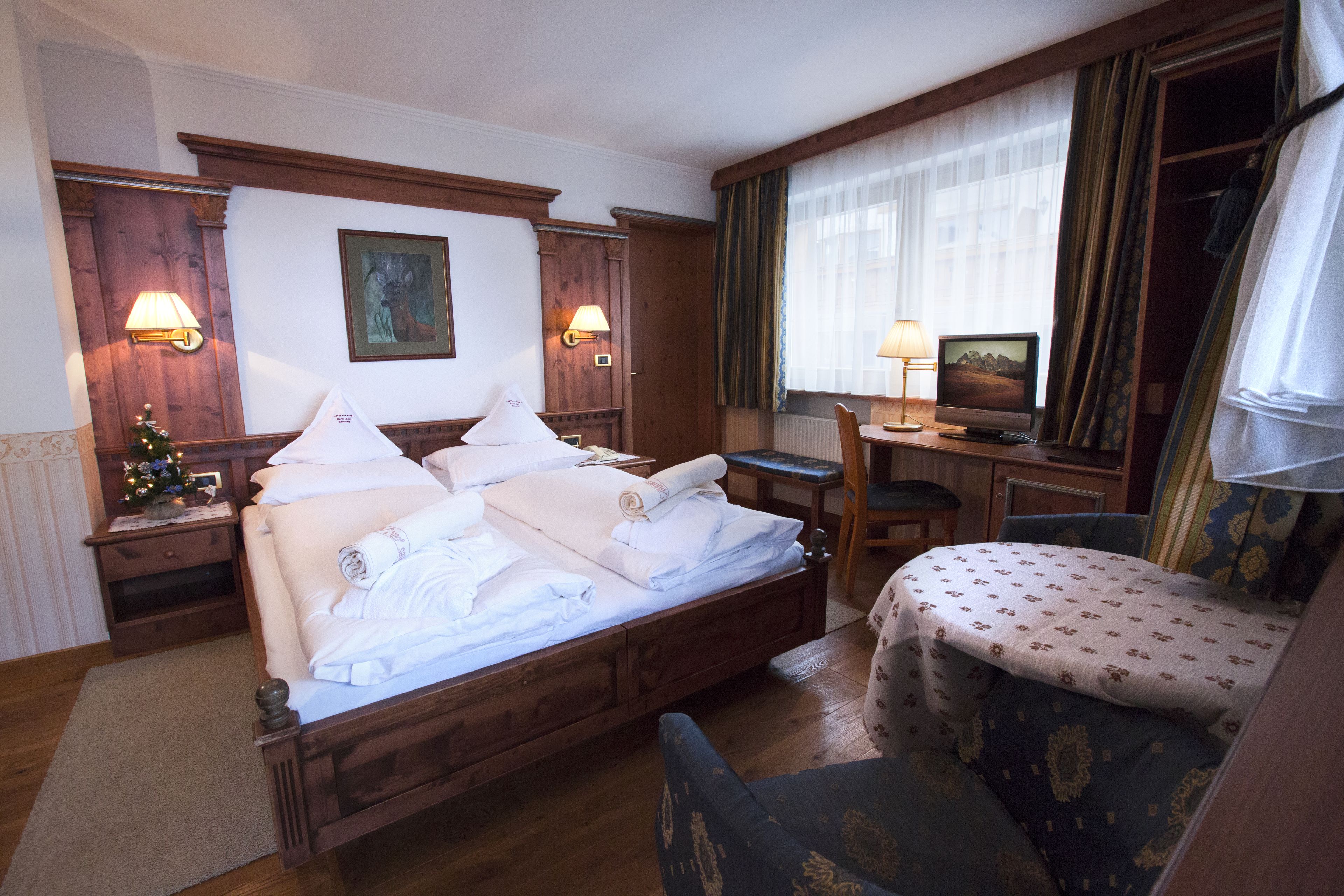 A hotel room with a wooden bed, two bedside lamps, a television, a small desk, and a chair.
