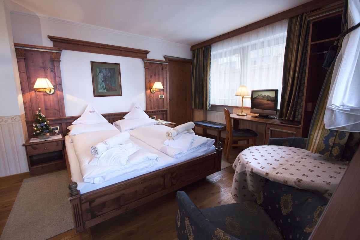 Une chambre d’hôtel avec un lit en bois, deux lampes de chevet, une télévision, un petit bureau et une chaise.