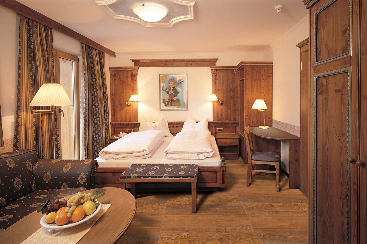 A hotel room with a bed, a desk, a chair, a sofa, and a table with fruit.