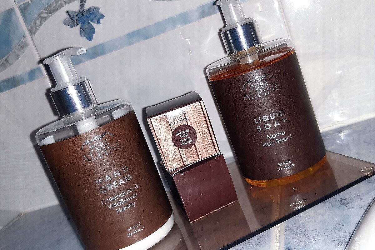 Three bottles of hand cream and liquid soap on a glass shelf.