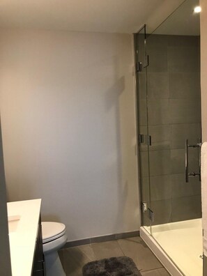 A modern bathroom with a toilet, a glass shower enclosure, and a bathtub. - Stay With Kay Pentagon City (Arlington)