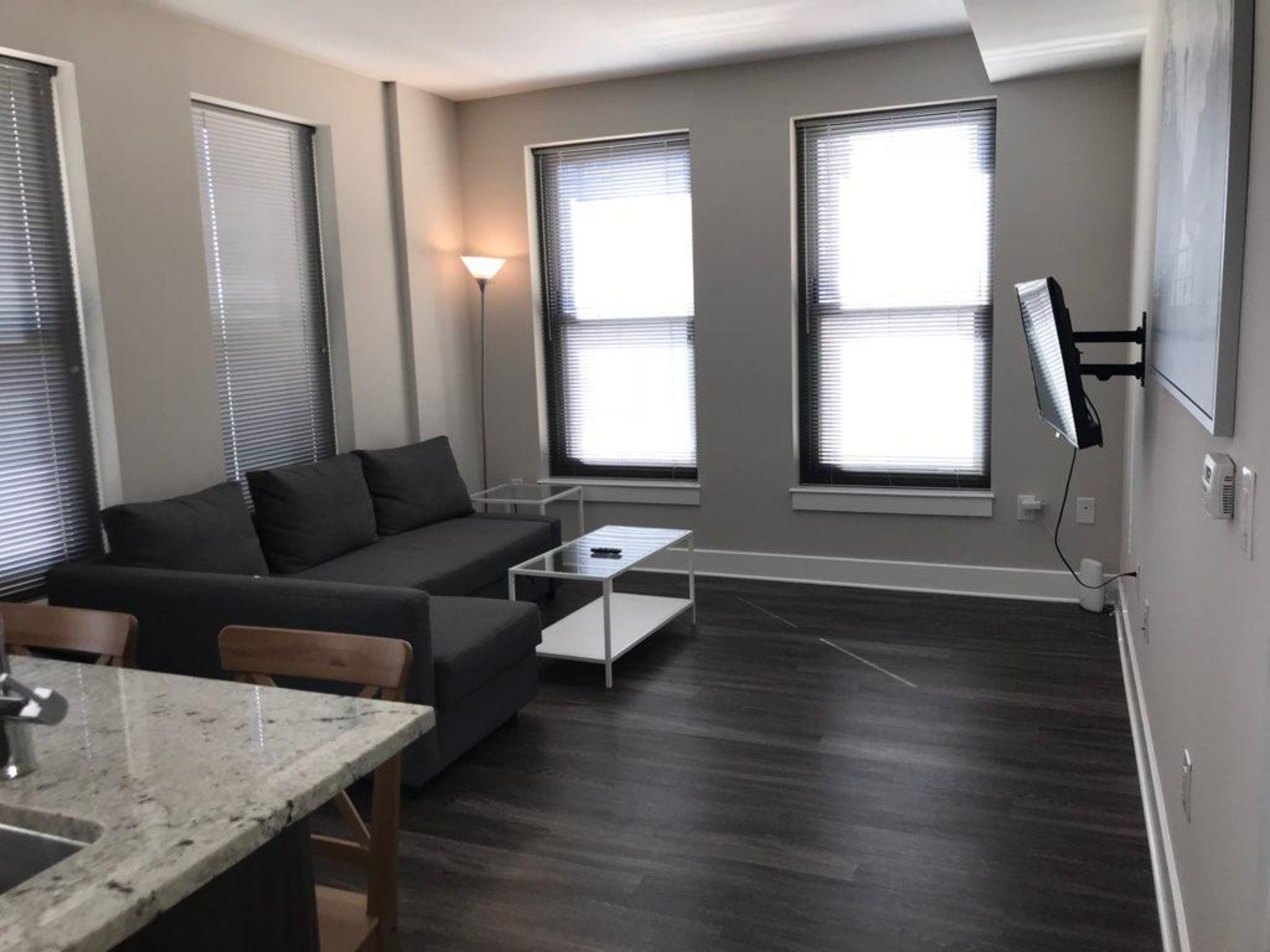 A modern living room with a grey sofa, a dining table, and a TV mounted on the wall.