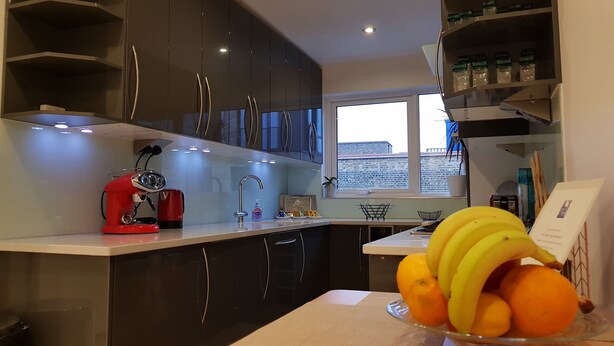 Uma cozinha moderna com armários escuros, uma cafeteira vermelha, uma pia e uma janela com vista para edifícios.