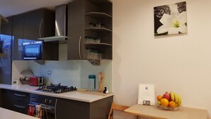 Cozinha moderna com armários escuros, micro-ondas embutido, fogão a gás e um pequeno espaço de jantar com uma fruteira.