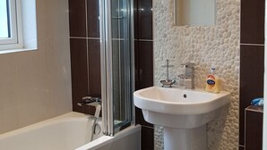 Um banheiro moderno com banheira, box de vidro, pia com espelho e vaso sanitário.
