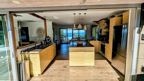 A modern kitchen with wooden cabinets, a central island, and a view of the ocean. - Holiday house right on Mollymook beach (Mollymook Beach)