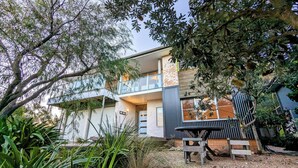 A two-story house with a balcony, surrounded by lush greenery. - Holiday house right on Mollymook beach (Mollymook Beach)