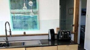 A kitchen with a modern design, featuring a stainless steel sink, a black toaster, and a glass backsplash. - Holiday house right on Mollymook beach (Mollymook Beach)