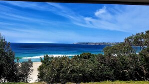 A coastal view with a clear sky, a sandy beach, and dense greenery. - Holiday house right on Mollymook beach (Mollymook Beach)