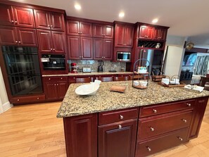 A kitchen with granite countertops, wooden cabinets, a built-in oven, a microwave, and a refrigerator.