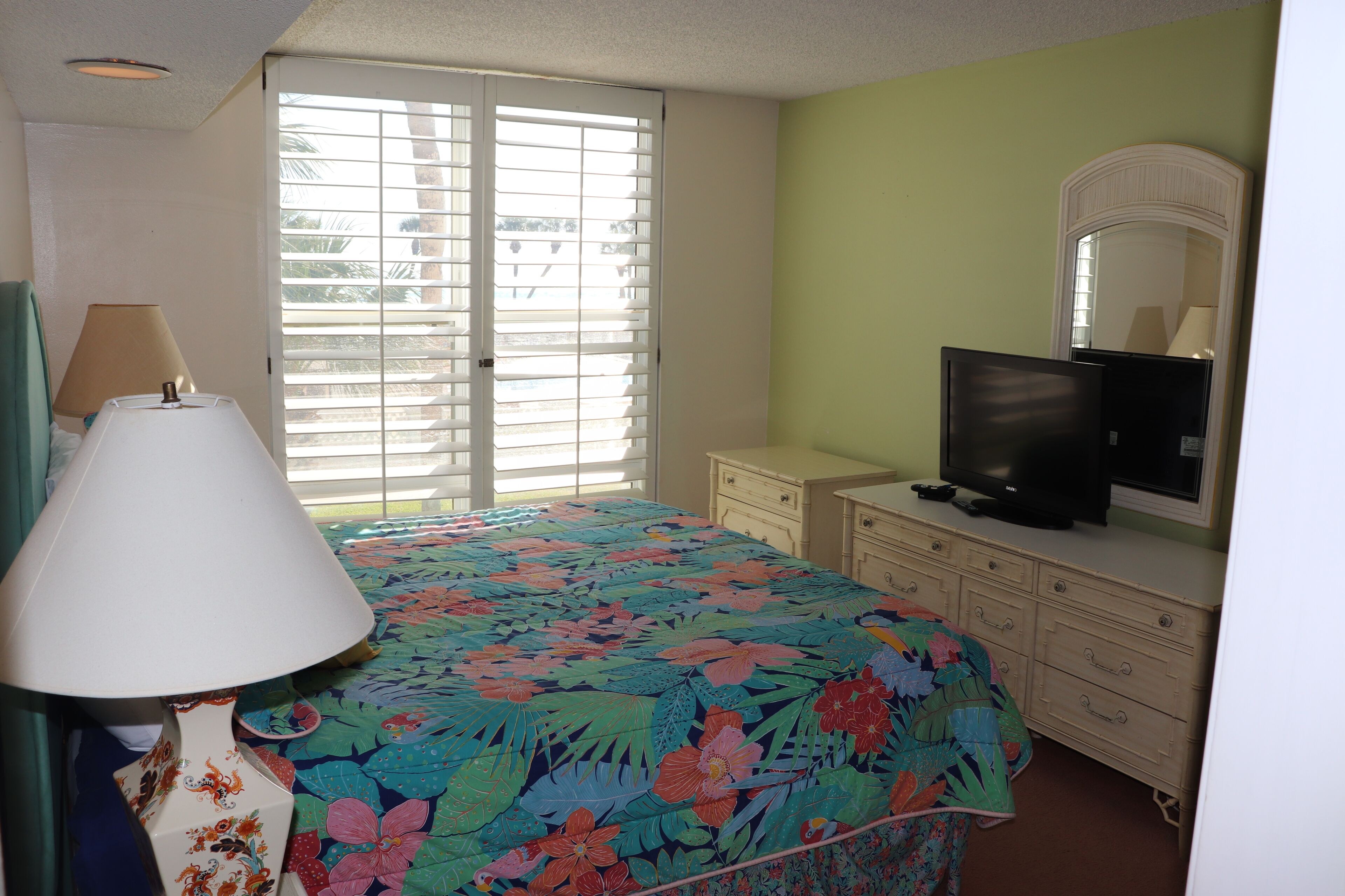 A bedroom with a bed, a dresser, a television, and a window with blinds.