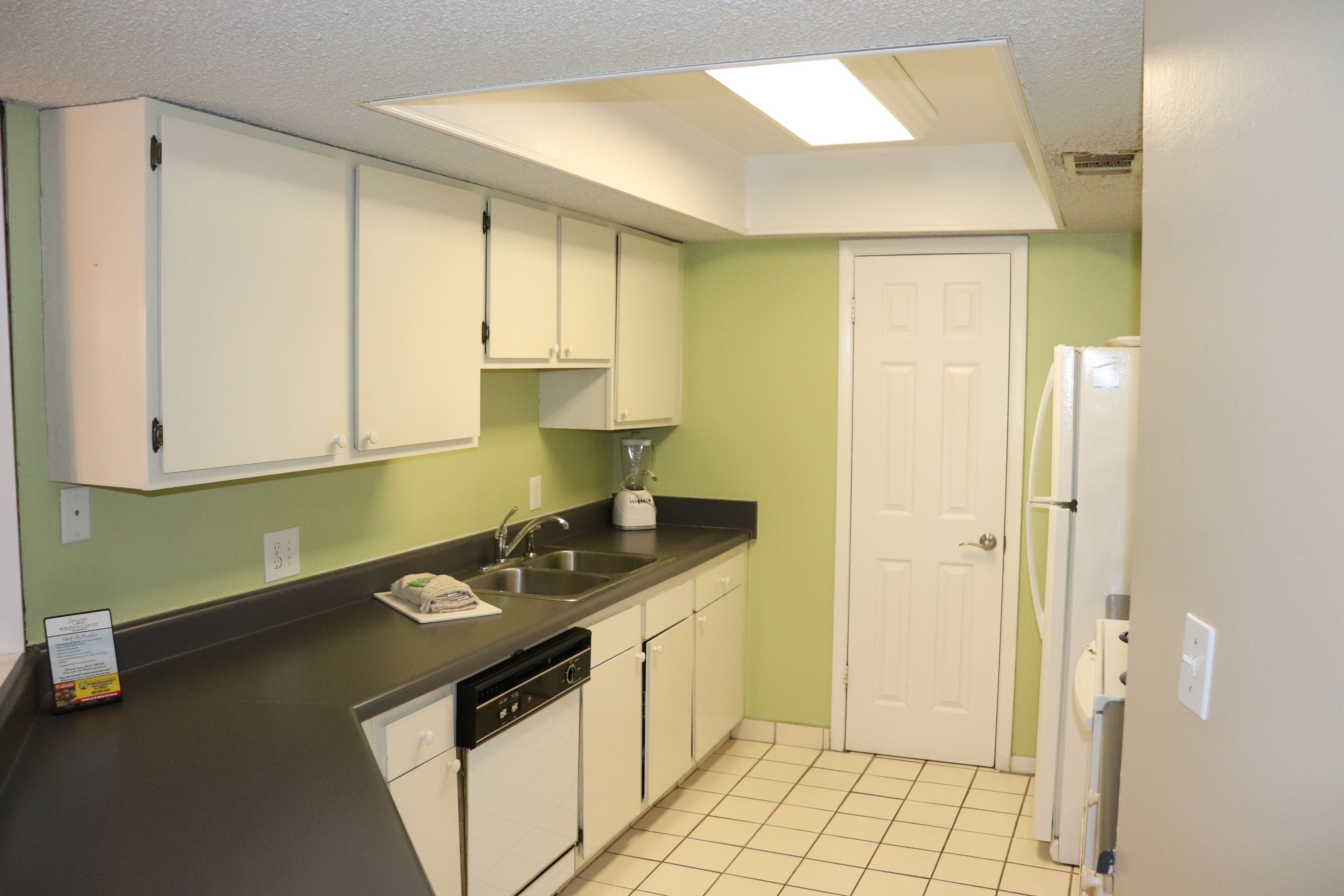 A compact kitchen with white cabinets, a black countertop, a dishwasher, and a refrigerator.