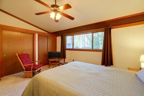 Une chambre d’hôtel avec un lit, un téléviseur posé sur un meuble, une chaise en bois et une fenêtre avec des rideaux.