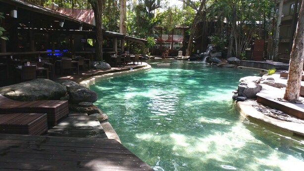Zona de piscina con cubierta de madera, rocas y un cartel de spa al fondo.