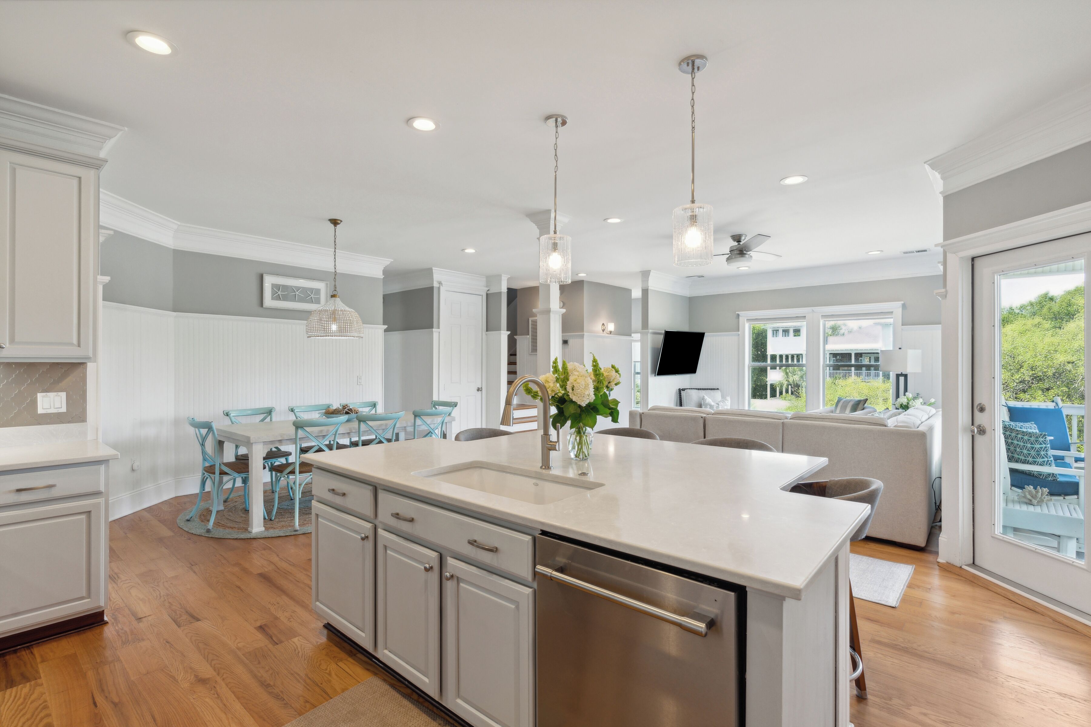 A modern kitchen with a large island, white cabinetry, and a dining area with blue chairs.