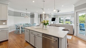 A modern kitchen with a large island, white cabinetry, and a dining area with blue chairs. - 3800 Cameron Boulevard| AvantStay | Pool, Ocean Views, Deck (Isle of Palms)