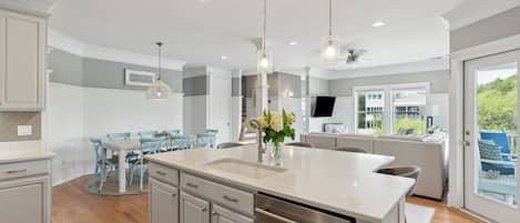 A modern kitchen with a large island, white cabinetry, and a dining area with blue chairs.