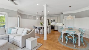 A spacious living area with a sofa, dining table, and chairs, a kitchen with white cabinets, and a ceiling fan. - 3800 Cameron Boulevard| AvantStay | Pool, Ocean Views, Deck (Isle of Palms)