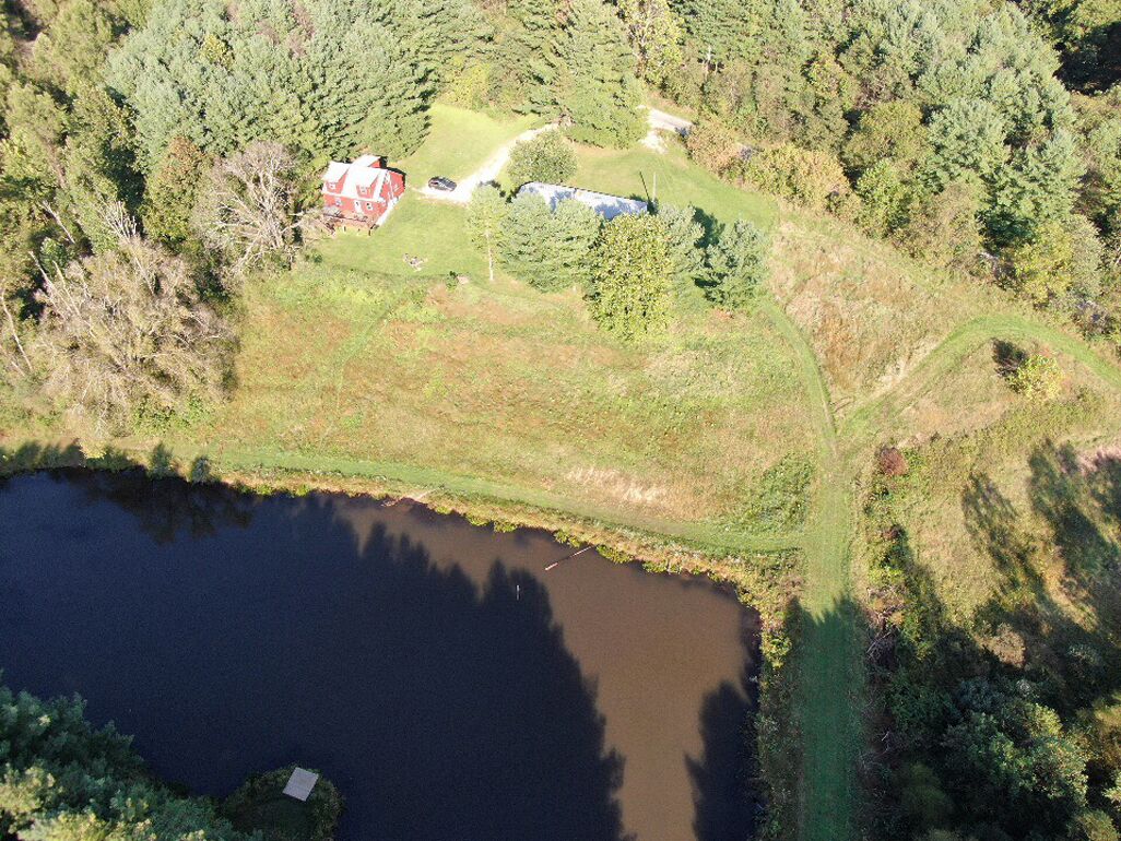 An aerial view of a property with a pond, a red building, and surrounding forest.