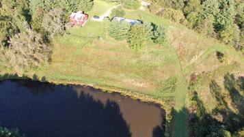 An aerial view of a property with a pond, a red building, and surrounding forest.