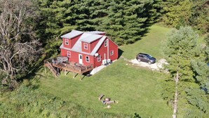 Uma casa vermelha de dois andares com um deck, rodeada por árvores densas e um gramado.
