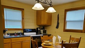 A kitchen with wooden cabinets, a dining table with chairs, and a hanging light fixture. - Hot Tub, Quiet, Relaxing , Fishing, Wi Fi, A.C., Fire Pit, Windy 9,  Hot Tub (Stewart)