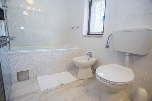 Ein Badezimmer mit Badewanne, Bidet, Toilette und einem Fenster mit Spitzenvorhang.