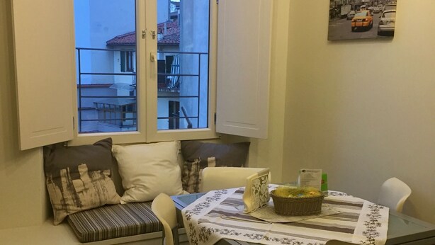 A dining area with a table set for two, a window with a view of buildings, and a wall-mounted picture. - Independent studio near Santa Maria Novella Train Station (Firenze)