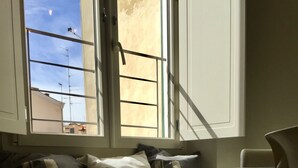 A room with a window seat, a chair, and a view of the sky and buildings outside. - Independent studio near Santa Maria Novella Train Station (Firenze)