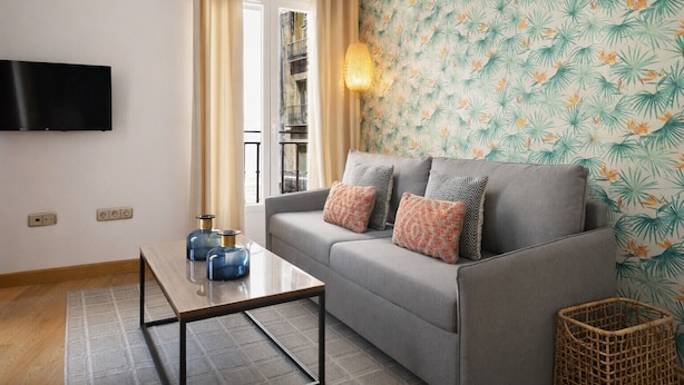 A modern living room with a grey sofa, two blue vases, a small table, and a wall-mounted TV. - Gran Vía II- Lovely apartment in the city center of Madrid (Madrid)