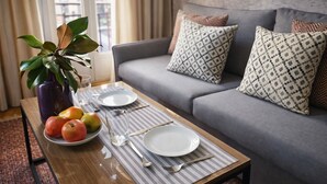 A dining table set with plates, cutlery, and fruit, positioned in front of a grey sofa with patterned cushions. - Gran Vía II- Lovely apartment in the city center of Madrid (Madrid)