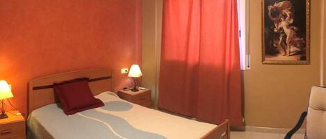 A hotel room with a bed, nightstands, a chair, a painting on the wall, and a window with curtains.